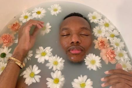 Person in bathtub half submerged, surrounded by floating flowers