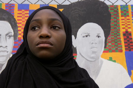 A Franklin High School student stands in front of a mural.