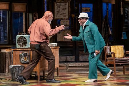 two men dressed in '70s clothes greet each other on stage