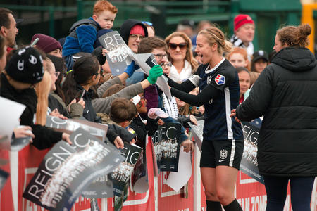 A Reign FC soccer player signs autographs for fans on the sideline.