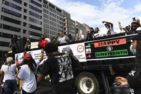 People stand on a flatbed truck that bears signs celebrating Juneteenth including one that reads "Happy Juneteenth" 