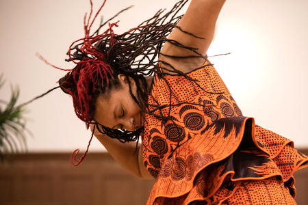 A woman in orange dances as her braids fly through the air