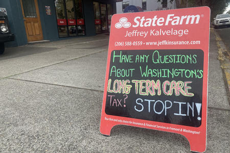 Sign on sidewalk inviting people to come into insurance broker's office to talk about the long term care act tax in WA 