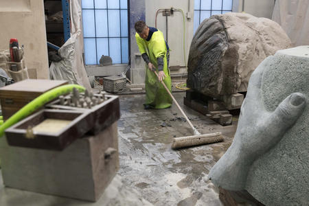 a man in a yellow safety vest sweeps up debris between sculptures in an art studio
