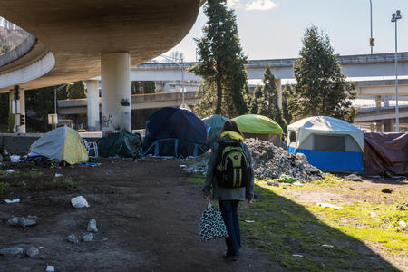A person walks among tents below a freeway overpass
