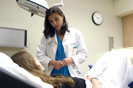 a woman doctor with dark brown hair leans over another woman lying back in a doctor's office