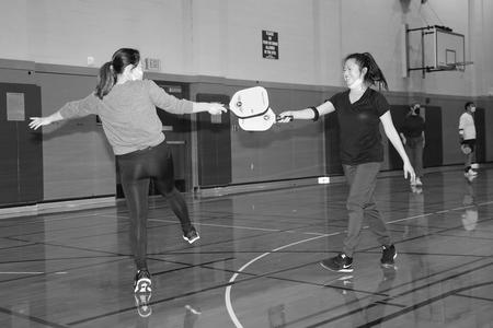 two players touch paddles on a pickleball court - black and white