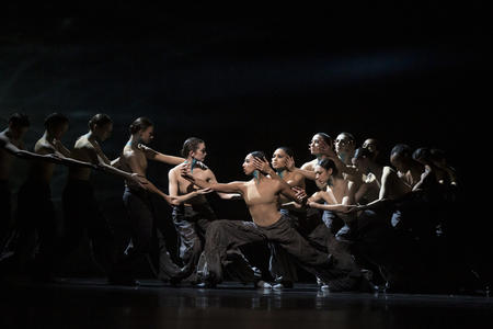 photo of performers on stage, two lines of dancers surrounding a central woman