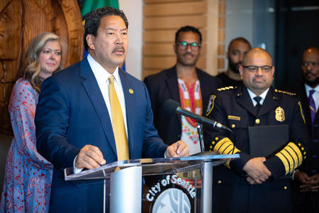 seattle mayor bruce harrell stands at a podium beside interim police chief adrian diaz 