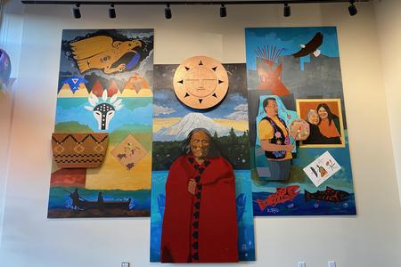 A three-panel mural with three-dimensional elements such as a wooden disk depict various people in earth tones on a blue background