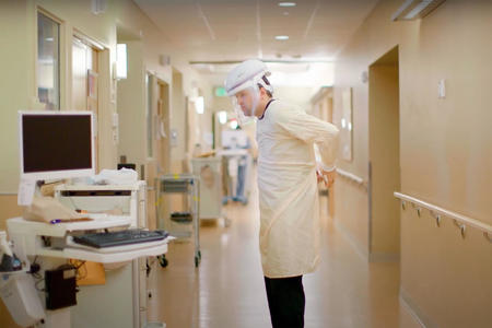 Nurse Paul Fuller ties a protective gown behind his back while wearing a face mask and other protective gear in a hospital hallway.