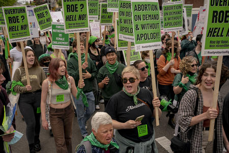 A crowd of demonstrators wearing green hold green signs reading 'abortion on demand and without apology'