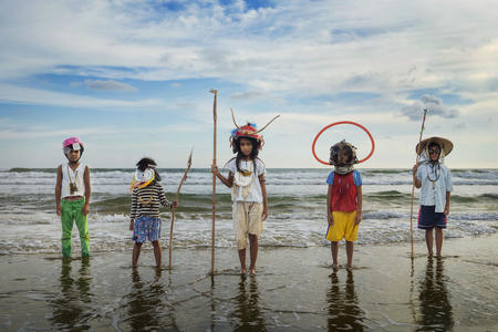 a row of children stands at the edge of the ocean, decked out in detritus