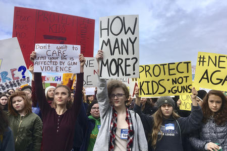 High school students in a demonstration hold signs with slogans such as "How many more?" and "Protect kids; not guns"