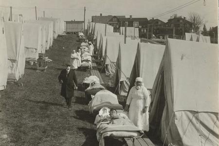 a black and white image of an emergency hospital, with tents and medical personnel as well as patients in beds
