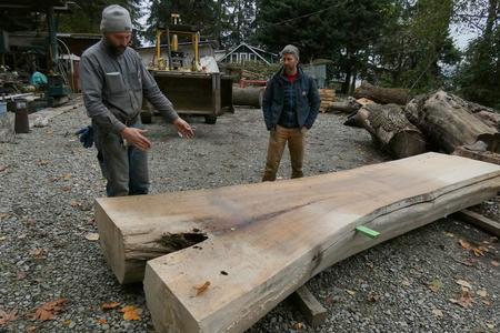 Two people stand over a planed slab of lumber