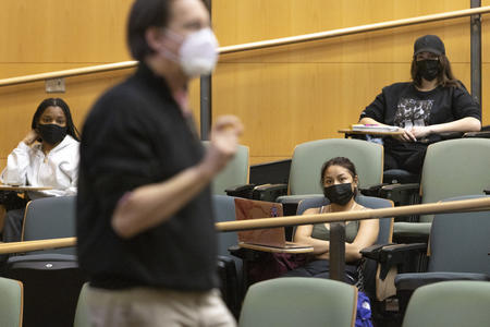 A man wearing a face mask walks in front of a lecture hall of students