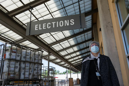 A woman wearing a face mask walks beneath a sign that reads "Elections"