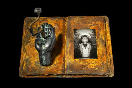 photo of an artwork -- an open book that appears to be covered in rust, with sculptural elements and a vintage photo inside