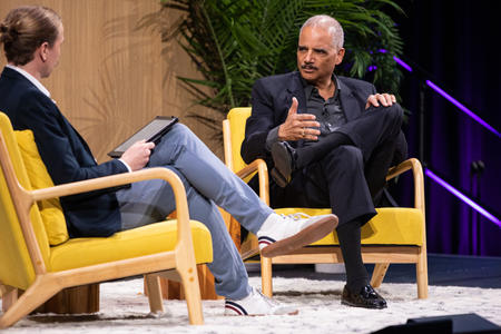 Two men sitting in yellow chairs on a stage, talking