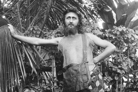 Black-and-white photo of a man in summer dress posing in a tropical area