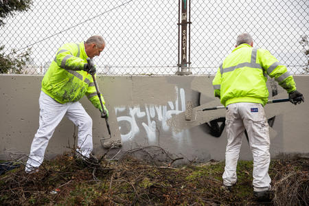 two men in neon yellow jackets paint over graffiti on a wall