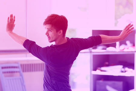 A man dances with his arms spread and his head looking towards the left; the image has a pink and purple color gradient