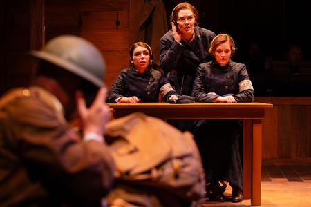photo of a stage play featuring three women in military uniform looking distressed