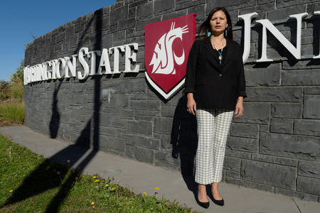 An adult stands and looks at the camera in front of a Washington State University sign