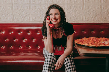 Rachel Belle poses next to a pizza and holds a telephone in her hand 