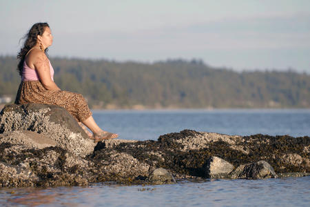 woman sitting on rock outcropping on ocean shore looking out at the water