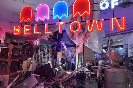 photo of a storefront with lots of junk piled inside and a neon sign with ghost figures