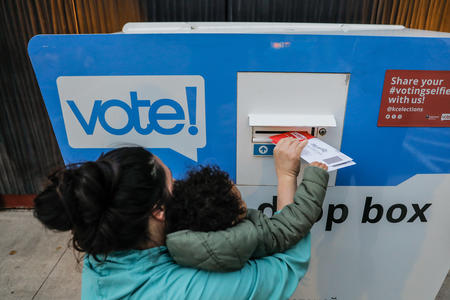 parent and child put ballots in a drop box