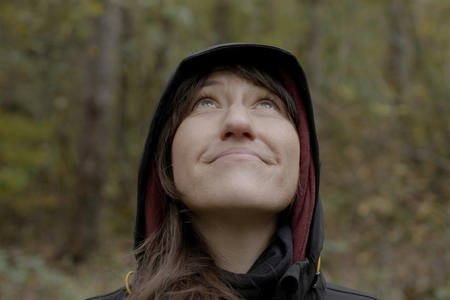 woman with raincoat on close up staring up at the sky with trees around her