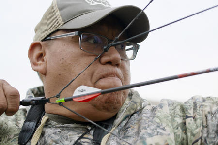 close up of man wincing and pulling back on hunting bow 