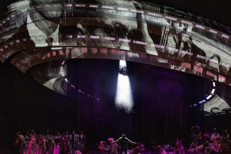 photo of a stage performance with a large gray spaceship appearing to "beam up" a man below