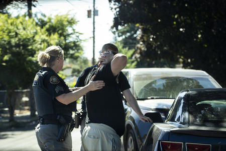 A police officer arrests a person and pats them down outisde a car.