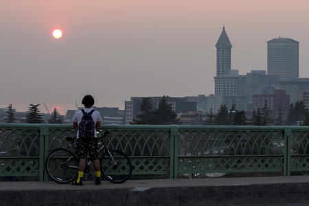 A man stands on a bridge in Seattle and looks at a smoky sunset 