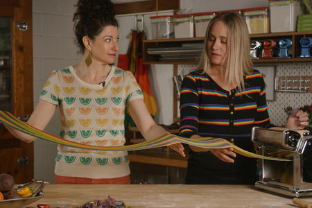 Host Rachel Belle holds a long sheet of rainbow pasta with her guest Linda Miller Nicholson
