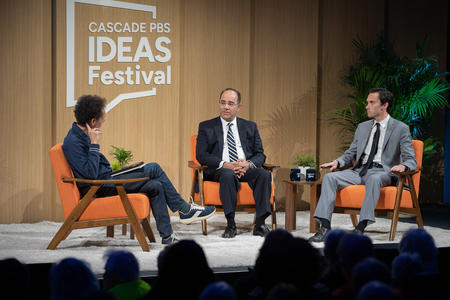 Three men sit on orange chairs on the Cascade PBS Ideas Festival stage