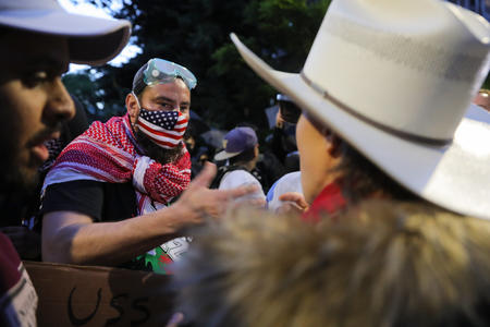 Person with a Palestinian scarf and American flag msk face off with another person wearing a cowboy hat.