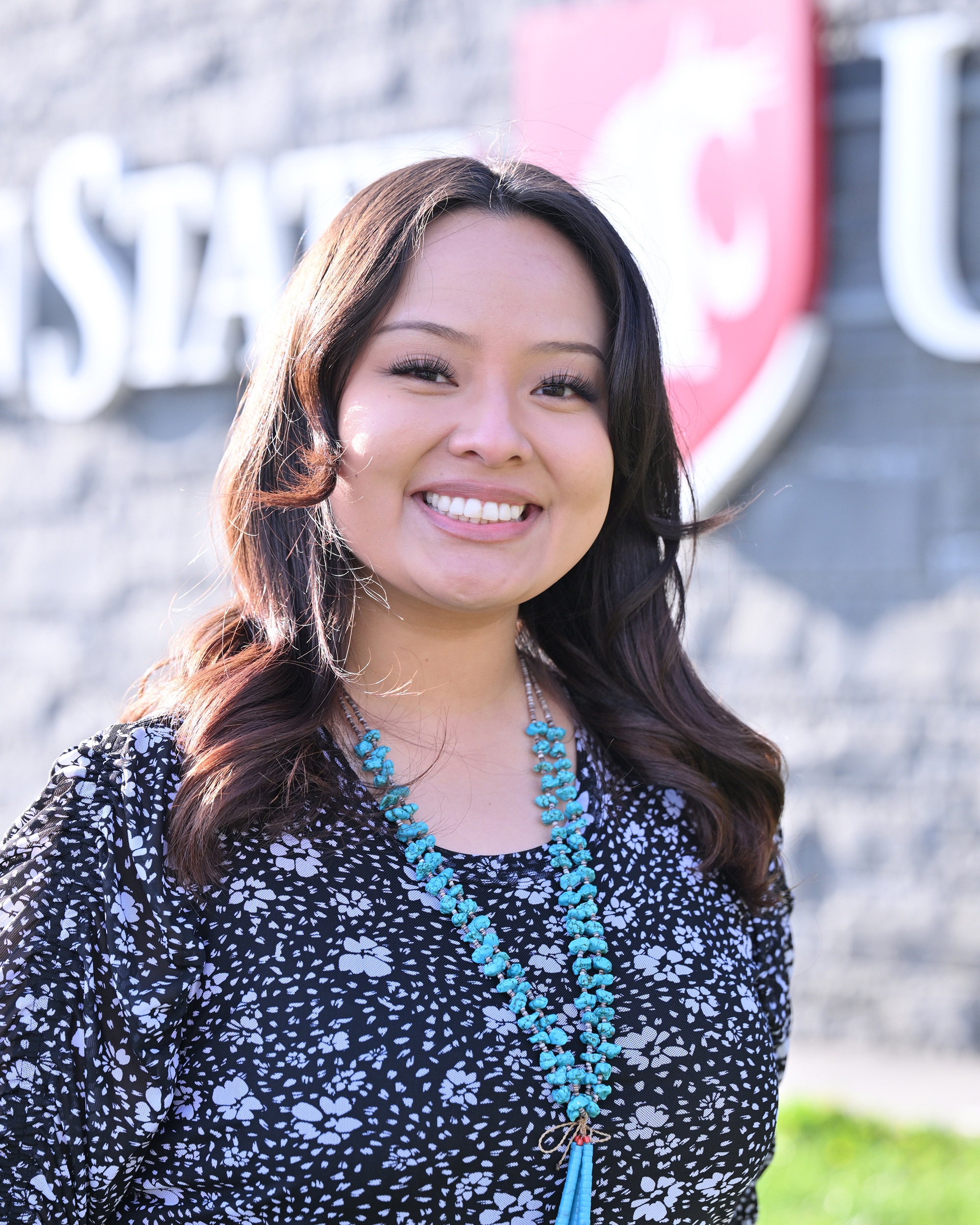 A person smiles at the camera in front of the Washington State University logo